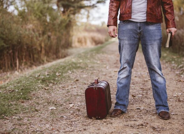 Male standing on an empty road near his old suitcase and holding the bible with blurred background