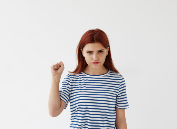 Aggressive young woman keeping her fist ready to fight and defend herself against injustice or violence. Strong woman showing pumped fist at camera as sign of girl power, feminism and independence