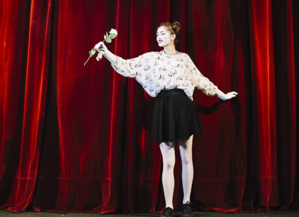 portrait-female-mime-standing-front-red-curtain-holding-white-rose
