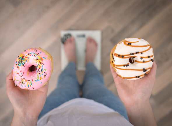 A woman stands on the scales, holds donuts in her hands, top view, copy space.