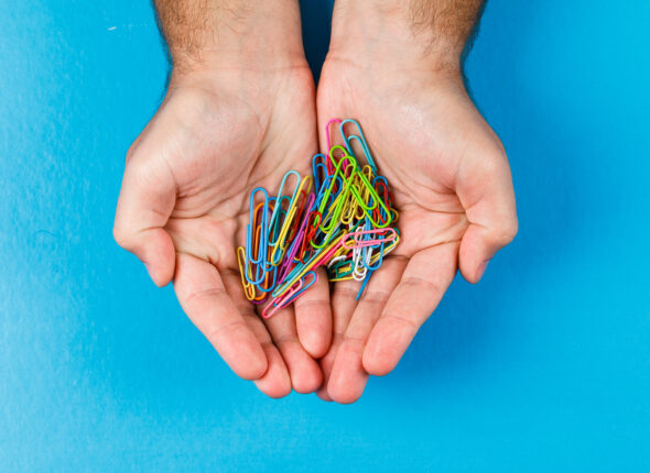Business and financial concept with paper clips on the palm on blue background flat lay.